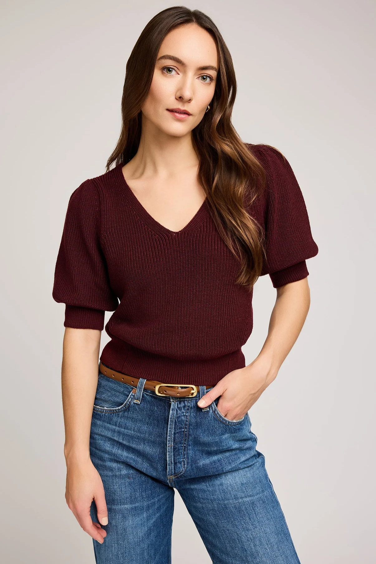 Woman wearing a burgundy sweater and blue jeans on a plain background