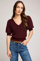 Woman wearing a burgundy sweater and blue jeans on a plain background