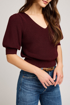 Woman wearing a burgundy sweater and blue jeans on a plain background