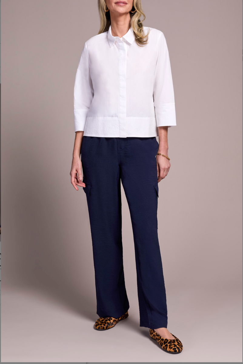 Woman wearing a white blouse and navy pants with leopard print shoes on a plain background