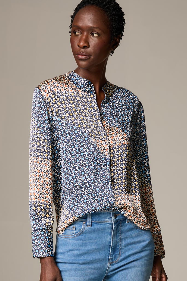Woman wearing a patterned blouse and blue jeans against a neutral background