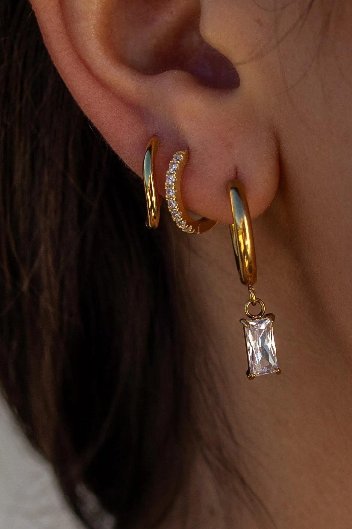 Close-up of a person's ear wearing gold hoop earrings with a central diamond pendant.