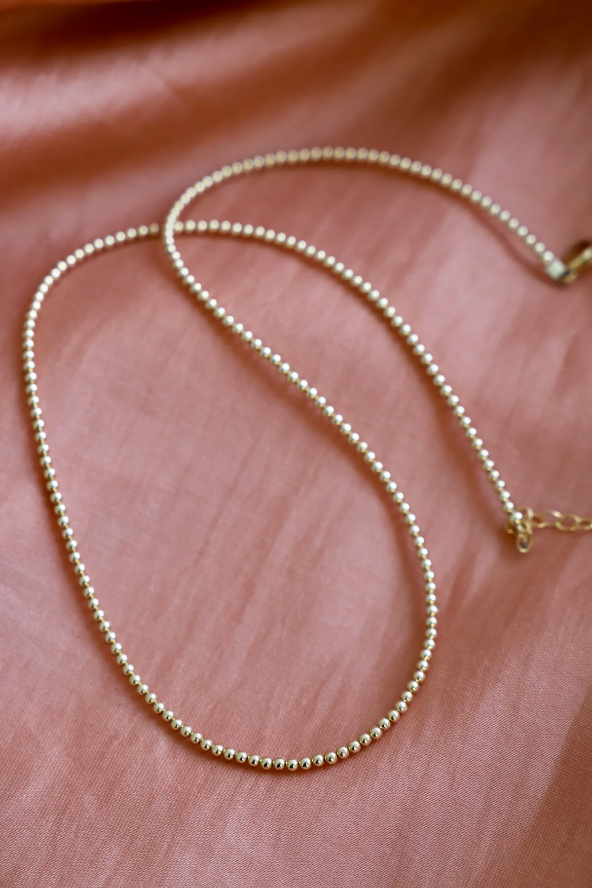 Gold necklace on a soft pink fabric background