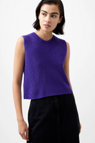 Woman wearing a purple sleeveless knitted top against a white background