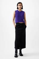 Person wearing a purple sleeveless top and black skirt on a white background