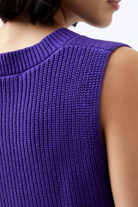 Close-up of a person wearing a purple knitted sleeveless top against a neutral background