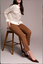 Woman sitting on a stool wearing a striped sweater and brown pants against a plain background