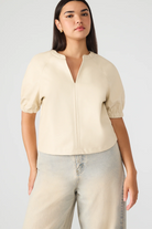 Woman wearing a beige short-sleeve blouse and light blue jeans on a white background