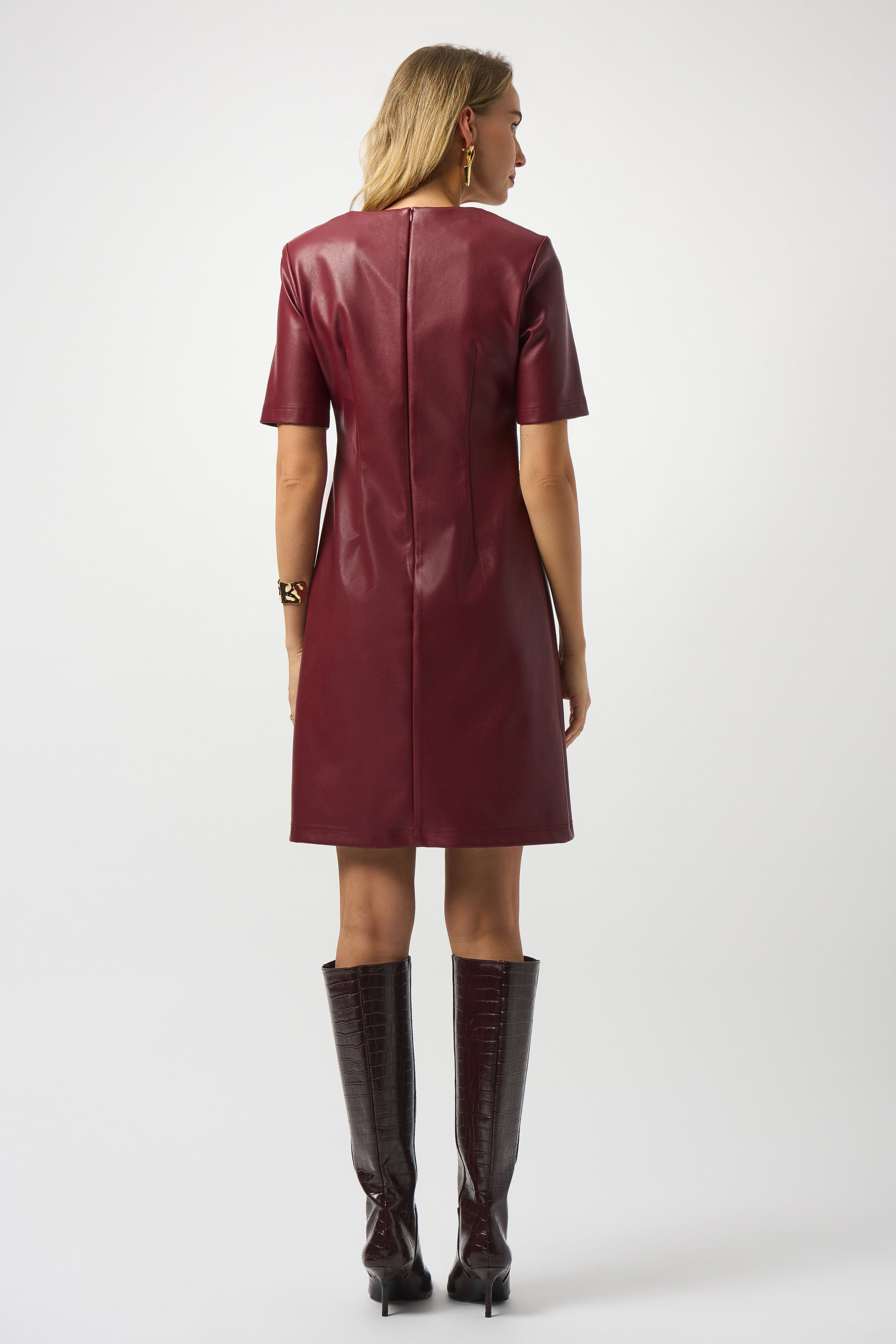 Woman wearing a burgundy leather dress with matching knee-high boots on a white background
