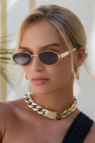 Woman wearing gold sunglasses and a gold necklace with a blurred background