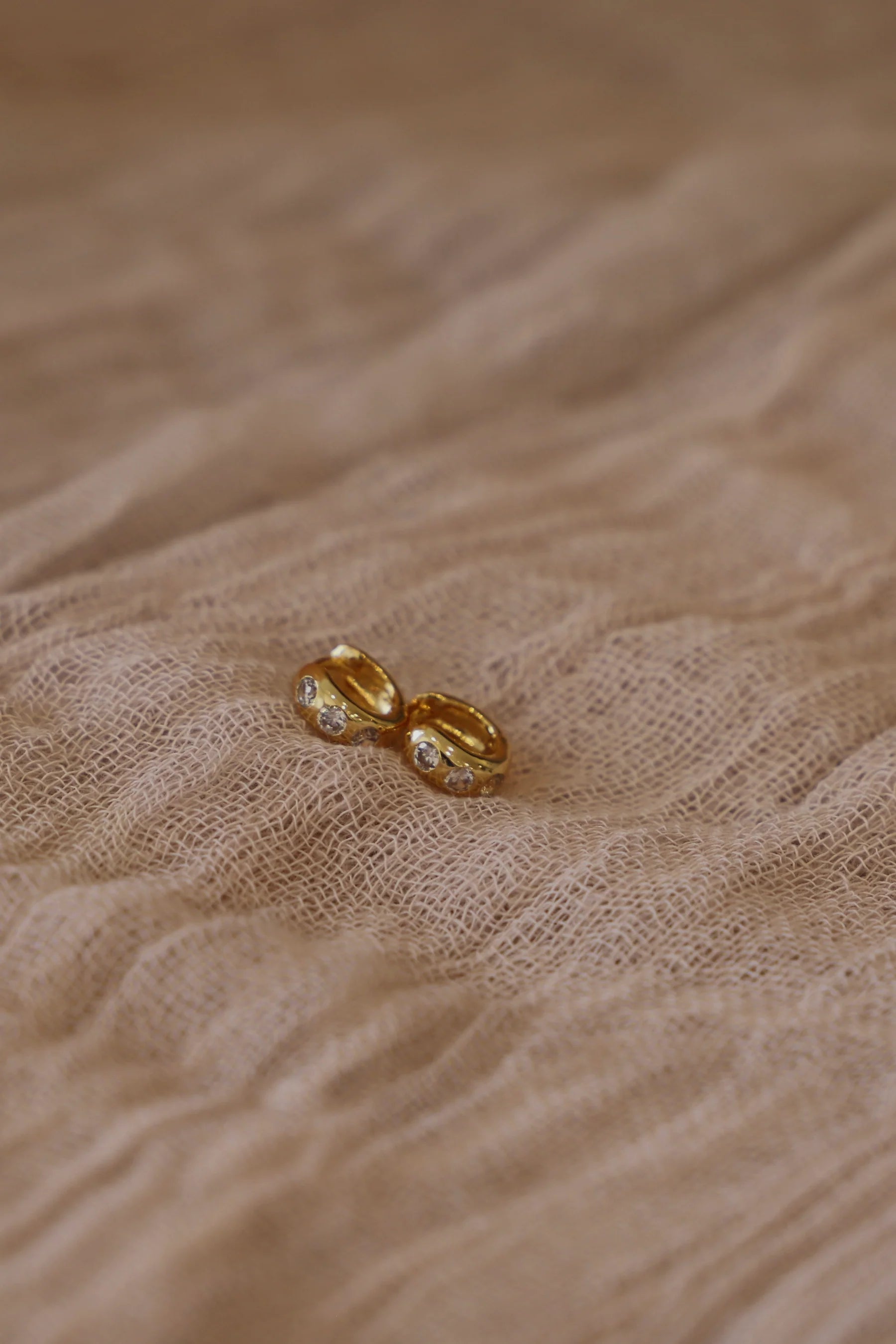 Gold earring on a textured beige fabric background