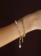 Two gold bracelets on a wrist against a dark background