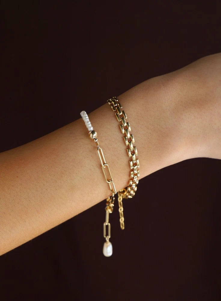 Two gold bracelets on a wrist against a dark background