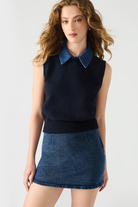 Woman wearing a navy sleeveless sweater with a denim collar and matching denim skirt on a white background