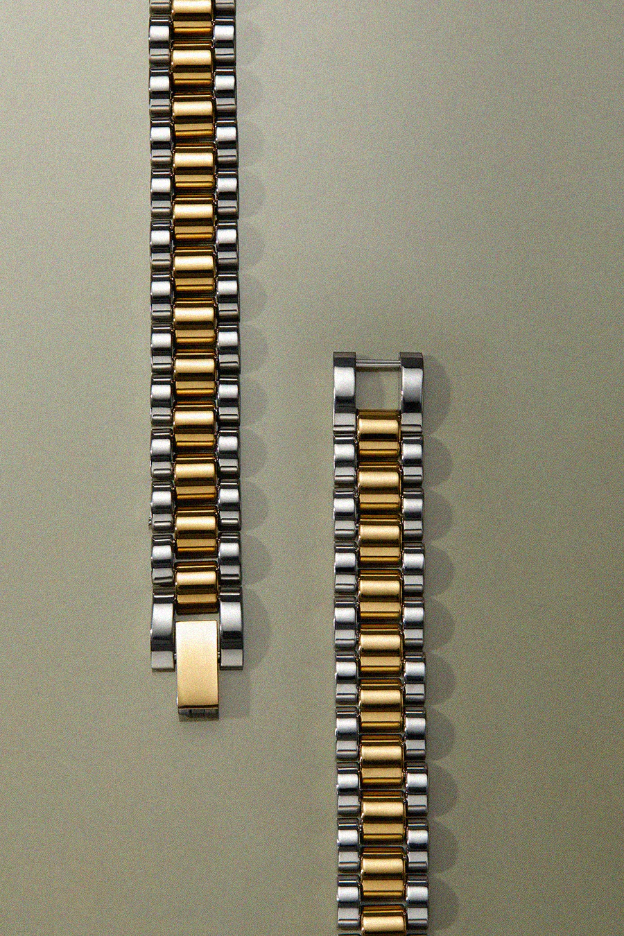 Two metallic watch straps, one gold and silver, the other gold and black, on a light gray background.