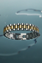 Two-tone silver and gold bracelet on a reflective surface