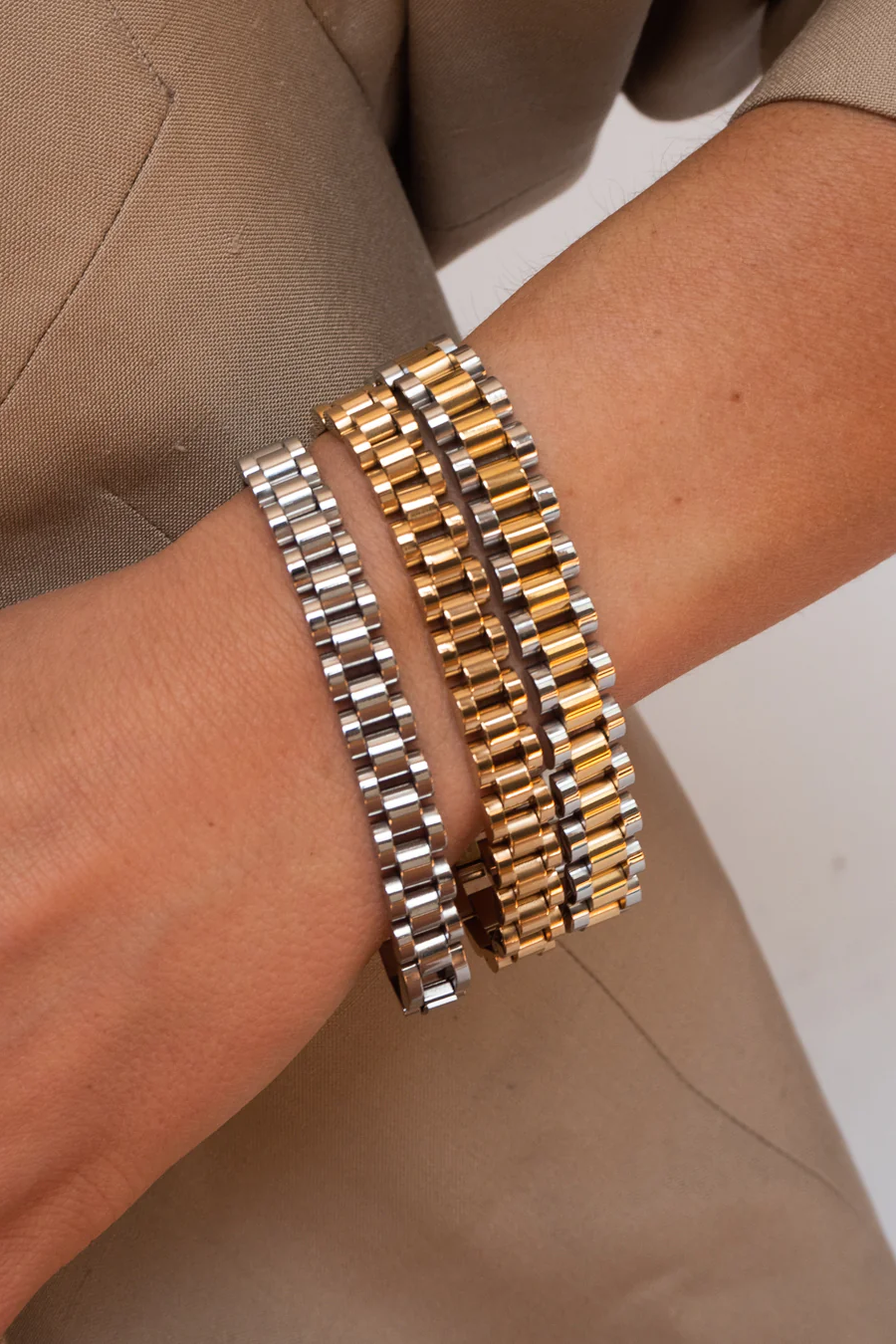 Close-up of a wrist wearing two metallic bracelets on a neutral background