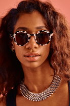 Woman wearing sunglasses and a necklace with a warm-toned background