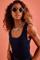 Woman wearing sunglasses and a dark blue sleeveless top against a pink background