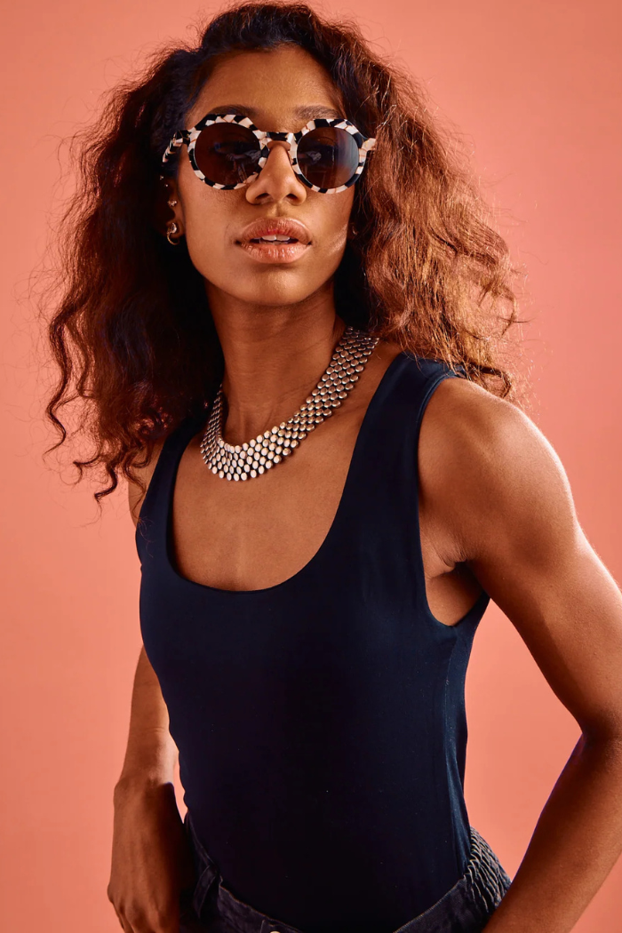Woman wearing sunglasses and a dark blue sleeveless top against a pink background
