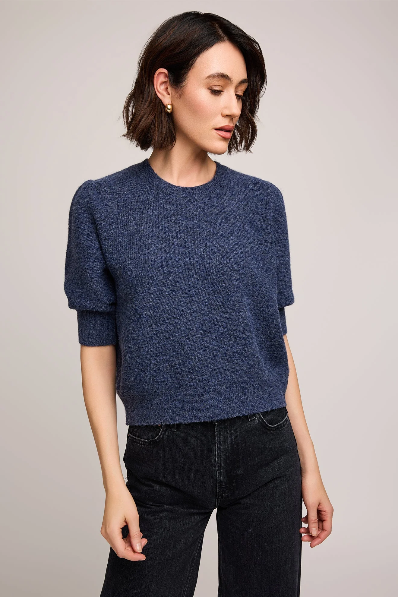 Woman wearing a blue sweater and black pants against a plain background