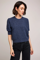 Woman wearing a blue sweater and black pants against a plain background
