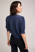 Woman wearing a blue sweater and black pants against a plain background