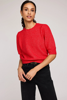 Woman wearing a red sweater and black pants against a plain background
