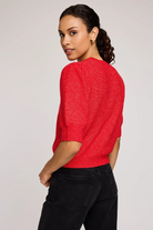 Woman wearing a red sweater and black pants on a plain background
