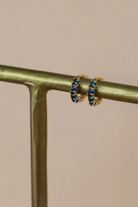 Gold hoop earrings with blue stones on a gold stand against a beige background