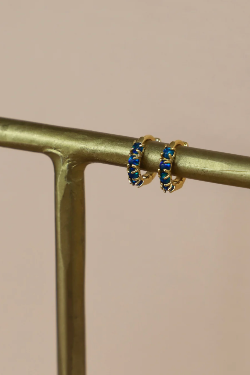 Gold hoop earrings with blue stones on a gold stand against a beige background