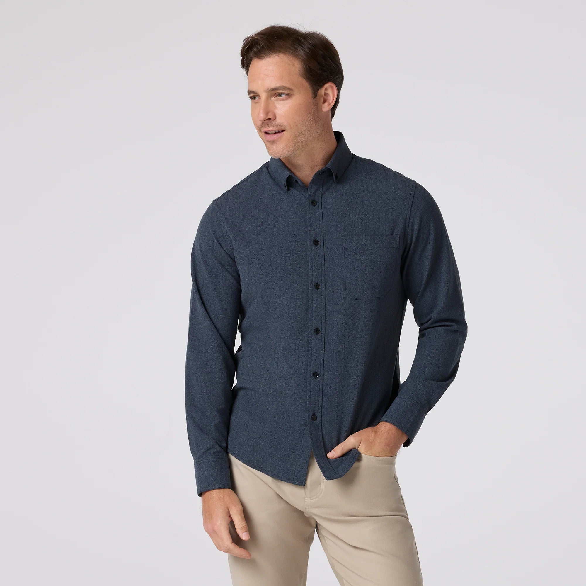 Man wearing a dark blue button-up shirt and beige pants on a light gray background