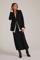 Woman wearing a black coat with white trim on a plain background