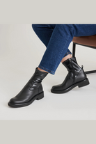 Person wearing black leather boots and blue jeans on a light gray background