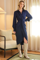 Woman wearing a blue dress with a slit standing in a room with a chair and lamp.