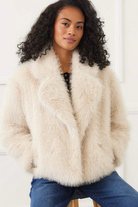 Woman wearing a fluffy beige coat against a white background