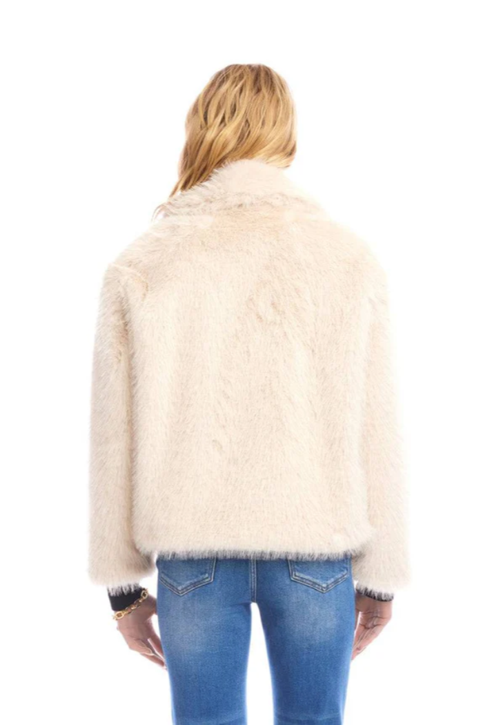 Person wearing a cream fur jacket and blue jeans on a white background