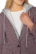 Close-up of a person wearing a textured purple coat with a gray hood and white shirt underneath.