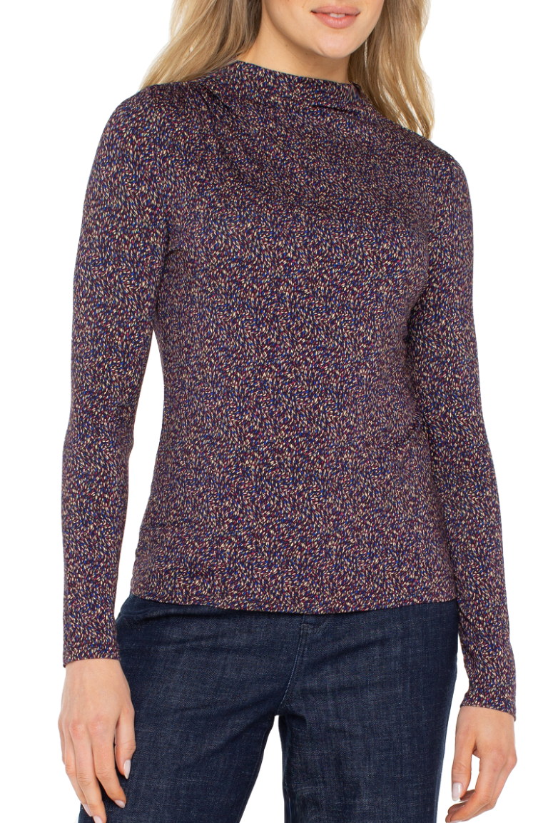 Woman wearing a patterned long-sleeve top and dark jeans on a white background