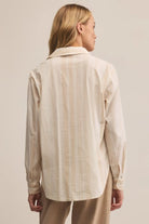 Woman wearing a beige striped shirt and pants against a plain background