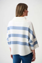 Woman wearing a white and blue striped poncho against a plain background