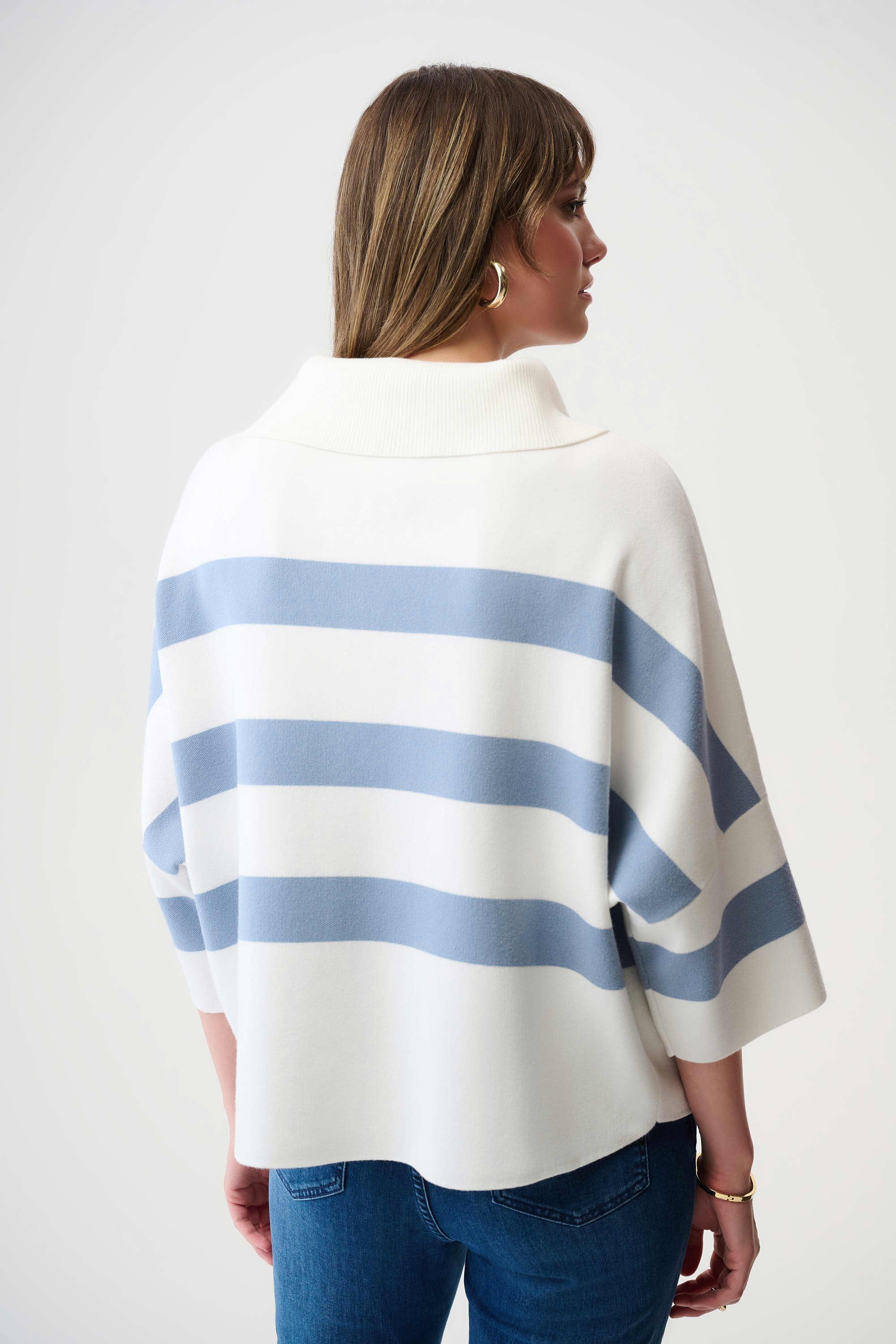 Woman wearing a white and blue striped poncho against a plain background