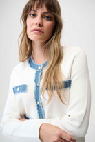 Woman wearing a white cardigan with blue denim accents on a plain background
