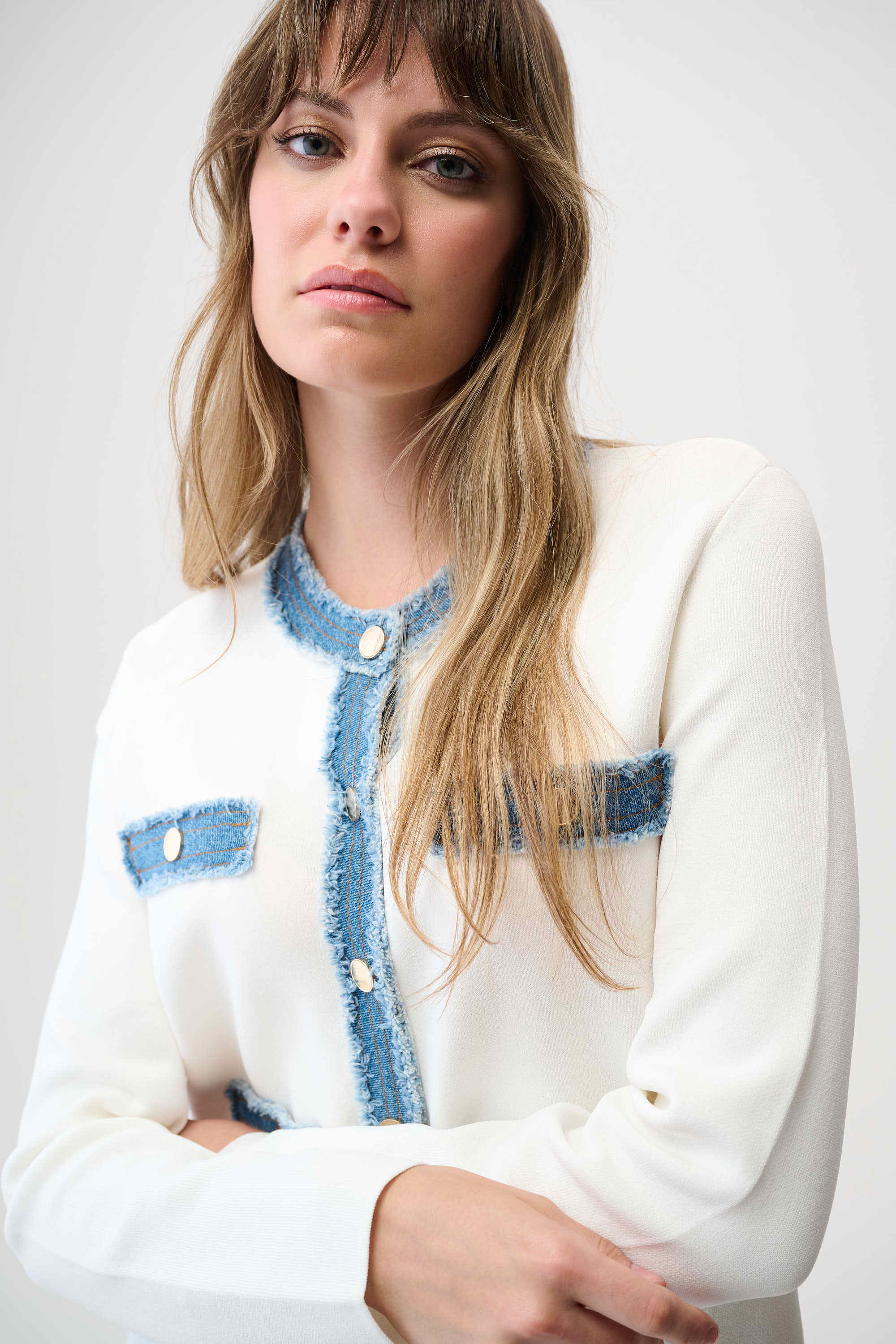 Woman wearing a white cardigan with blue denim accents on a plain background