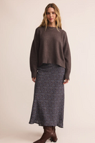 Woman wearing a brown sweater and patterned skirt on a beige background