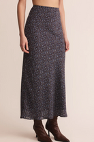 Person wearing a long, dark patterned skirt with brown boots on a beige background