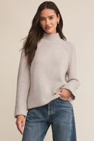 Woman wearing a light gray sweater and blue jeans on a beige background