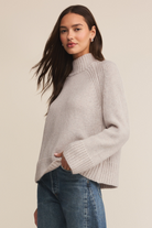 Woman wearing a light gray sweater and blue jeans against a beige background
