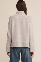 Person wearing a beige ribbed sweater and blue jeans on a beige background