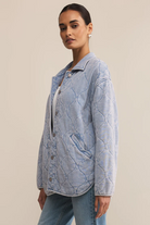 Woman wearing a light blue quilted jacket against a beige background